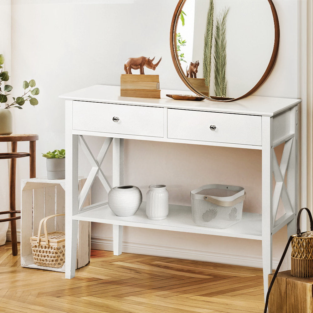 White console table with two drawers, X-frame sides and lower shelf, styled with vases and rhino figurines in entryway