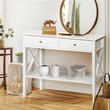 White console table with two drawers, X-frame sides and lower shelf, styled with vases and rhino figurines in entryway
