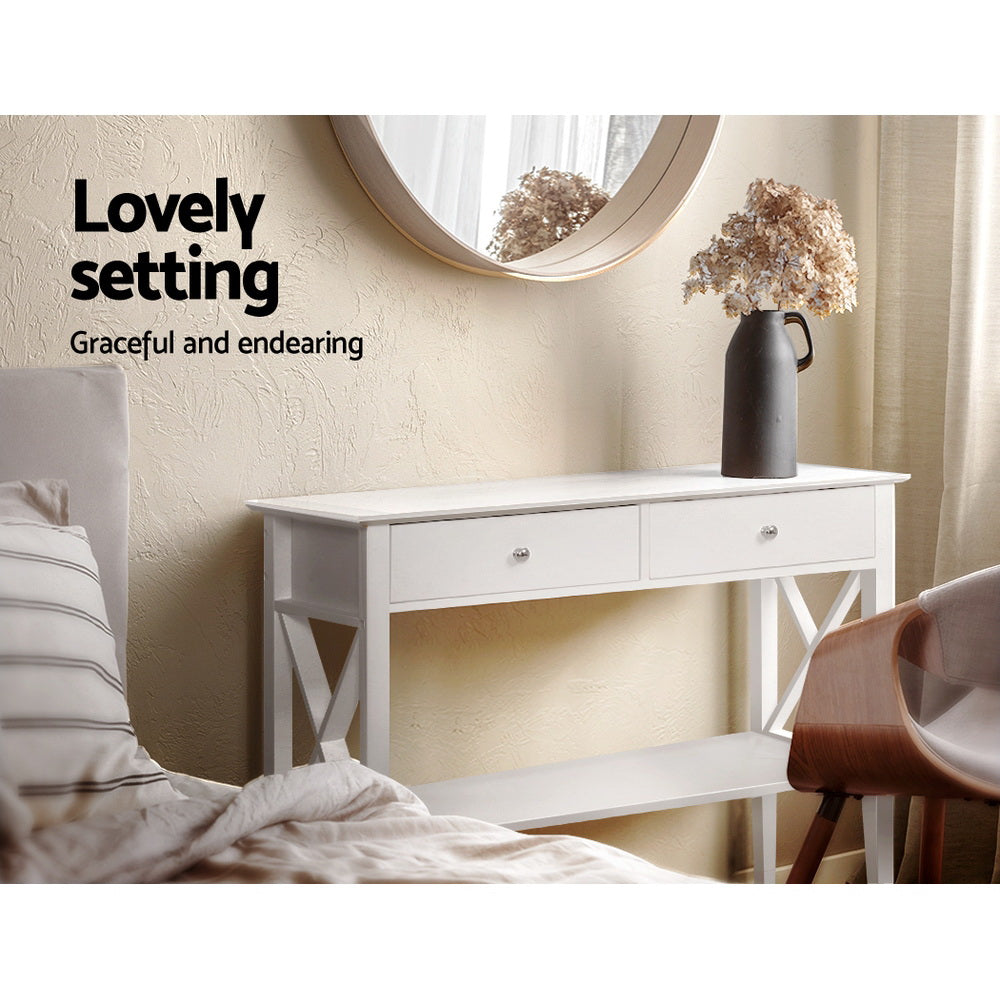 White console table with X-frame sides in bedroom, styled with dark ceramic vase and dried flowers; text "Lovely setting"