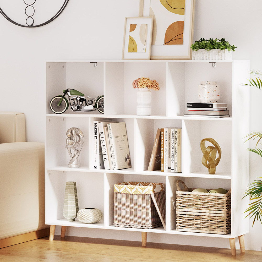 White low cube bookshelf with nine open compartments on angled wood legs, styled with books and baskets in living room