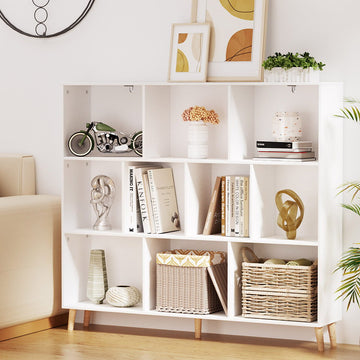 White low cube bookshelf with nine open compartments on angled wood legs, styled with books and baskets in living room