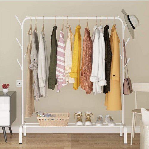 White garment rack in home setting loaded with neutral and yellow toned autumn clothes with basket on bottom shelf