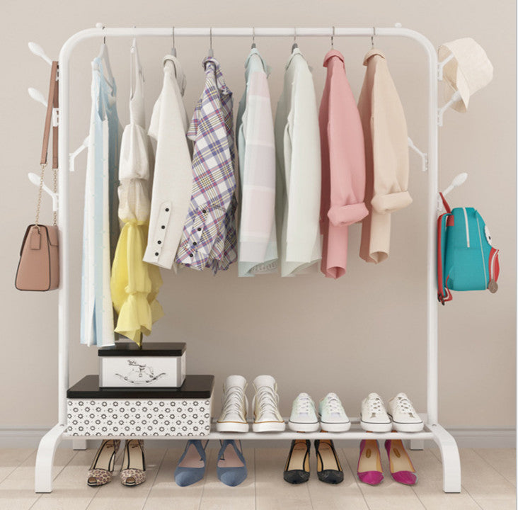 White steel garment rack with branch hooks loaded with pastel clothes and bags with shoes and box on bottom shelf