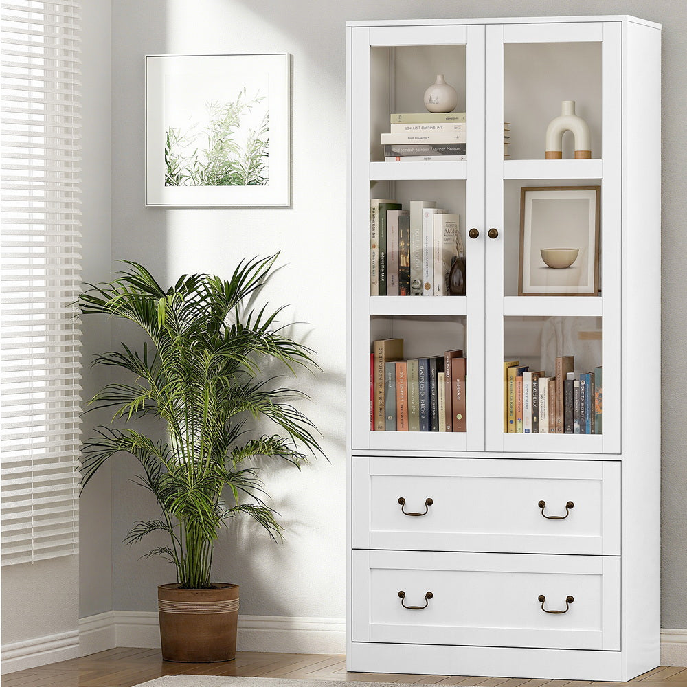 White tall display cabinet in living room, frosted glass doors open showing shelves with books and vases, two drawers below