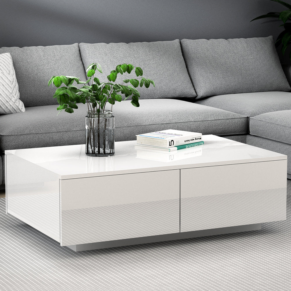 White high-gloss coffee table with two front drawers in living room setting with grey sofa behind
