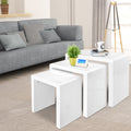 Three white high-gloss nesting tables spread at varying heights in living room, plant and photo frame on middle table
