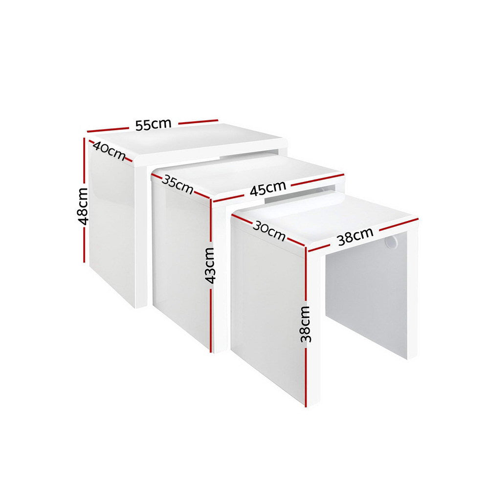 Set of three white high-gloss nesting tables in living room with grey sofa, plant and photo frame on top