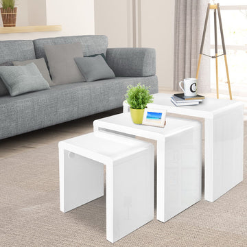 Set of three white high-gloss nesting tables in living room with grey sofa, plant and photo frame on top