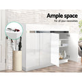 White gloss 3-door shoe cabinet in hallway setting with one door open showing shelves against brick wall