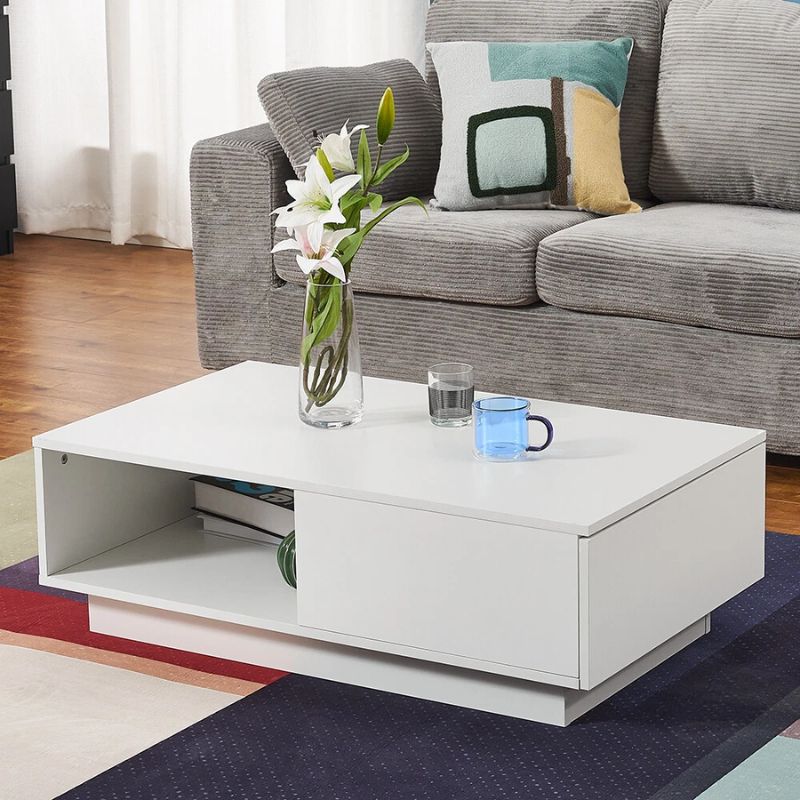 White high-gloss coffee table in living room, open shelf with orange LED lighting and books, beside grey sofa and blue wall