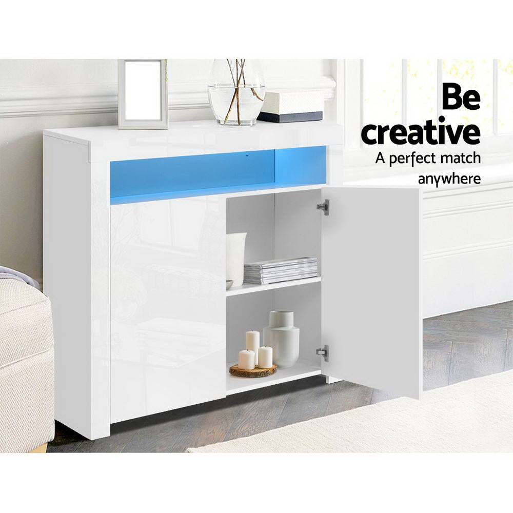 White LED sideboard in living room with one door open showing two shelves with candles and books, blue LED strip lit