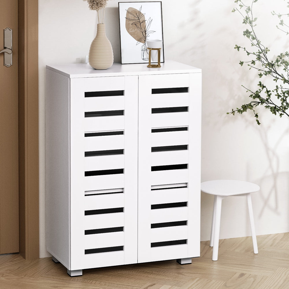 White louvred 2-door shoe cabinet in hallway with vase and art print on top and white stool beside