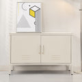 White metal two-door locker cabinet with vent slots on thin legs in living room setting with geometric art print on top