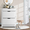 White shoe cabinet with oak top three flip-out doors in hallway with round mirror plant lamp and silver heels on rug