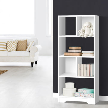 White tall asymmetric open bookcase styled with stuffed rabbit and storage boxes against dark wall in living room