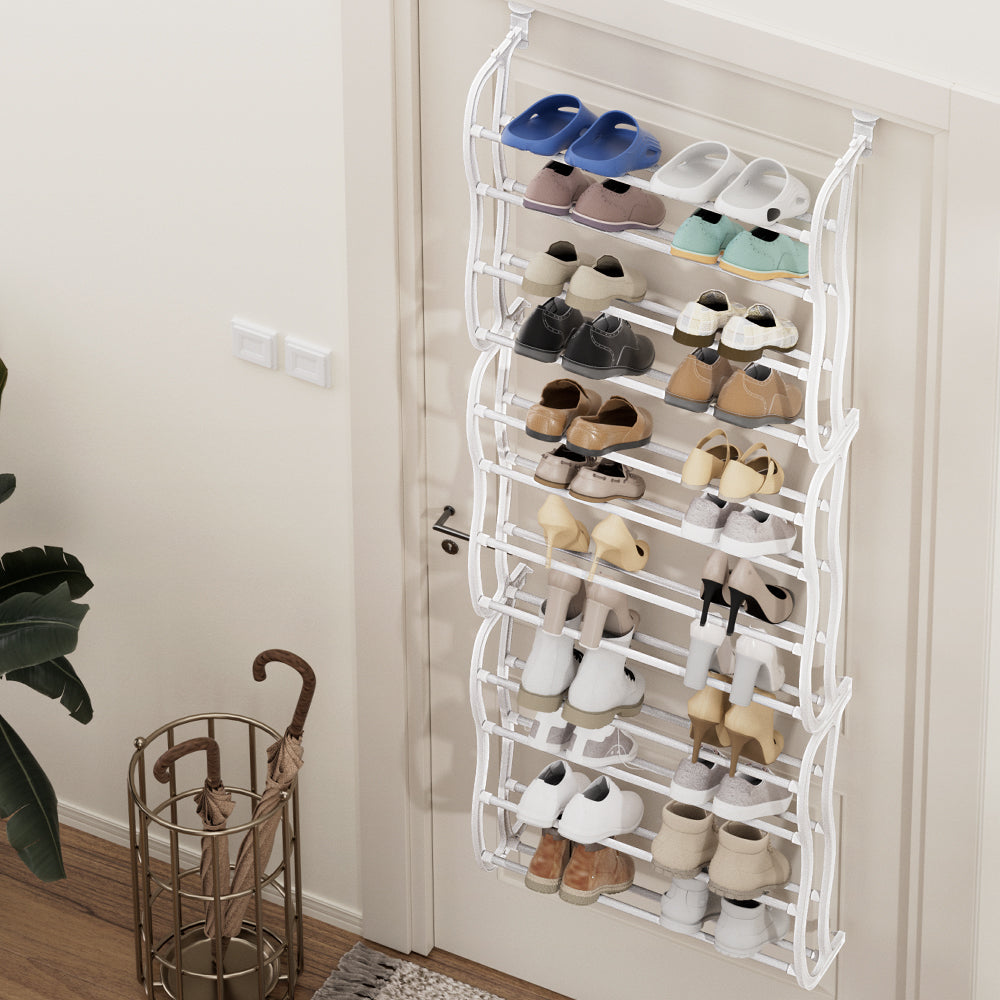 White over-door shoe rack with 12 tiers fully loaded with shoes mounted on door in hallway with umbrella stand and plant