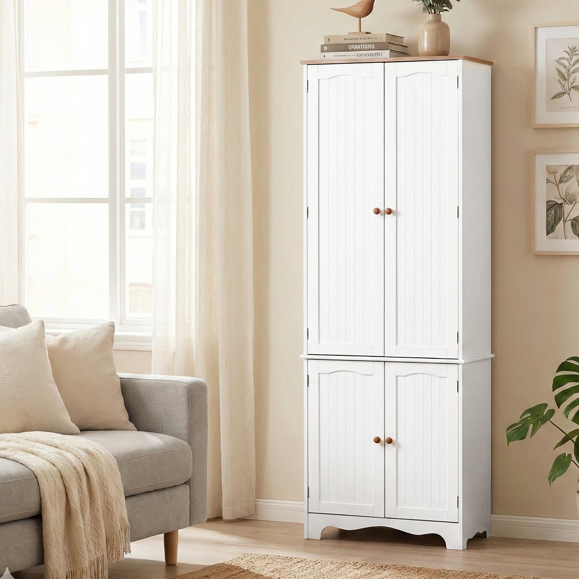 White pantry cabinet with doors closed in living room, top styled with books and vase, sofa and botanical prints visible