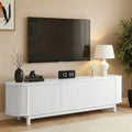 White fluted TV unit with rounded ends and 4 ribbed doors below mounted TV with clock lamp and plant