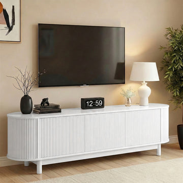 White fluted TV unit with rounded ends and 4 ribbed doors below mounted TV with clock lamp and plant