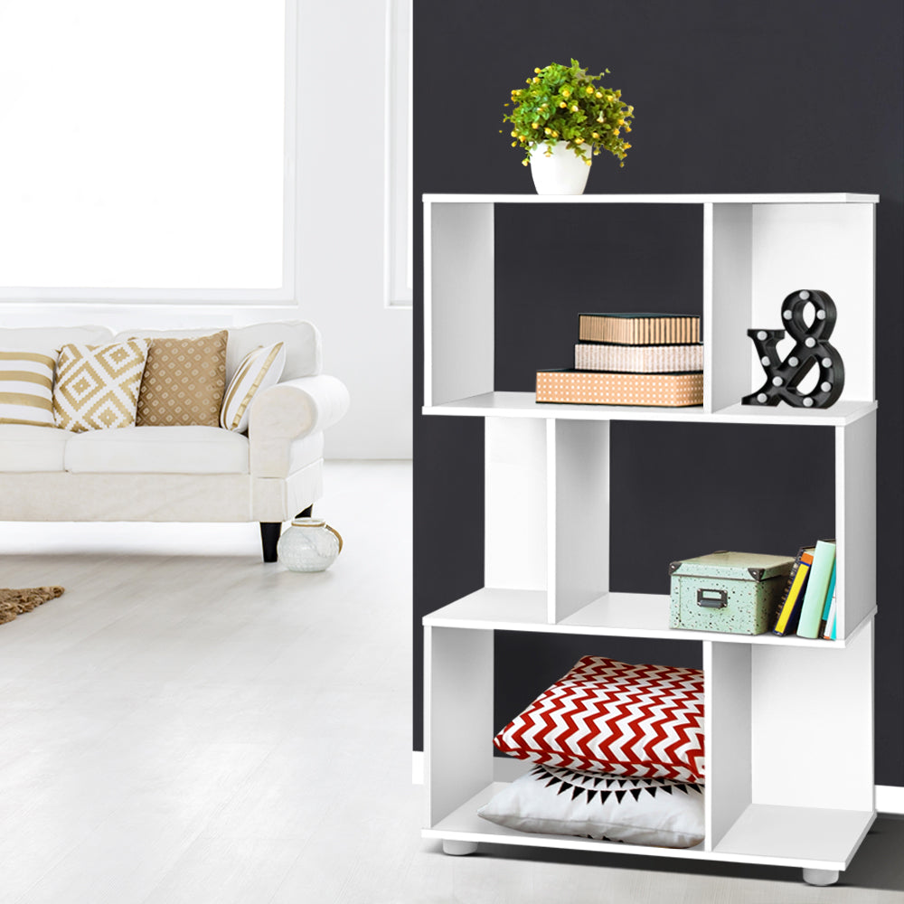White S-shaped 3-tier shelf beside dark wall styled with plant and books, red chevron cushion in base, white sofa visible