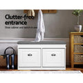 White shoe bench with two cup pull handle doors closed grey cushion in hallway lifestyle with coat rack and boots on floor