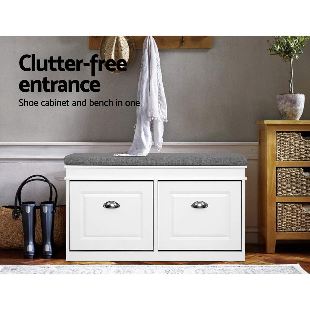 White shoe bench with two cup pull handle doors closed grey cushion in hallway lifestyle with coat rack and boots on floor