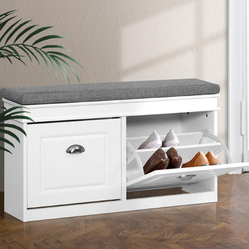 White shoe bench with grey fabric cushion left door closed and right flip-out compartment open showing shoes on parquet floor