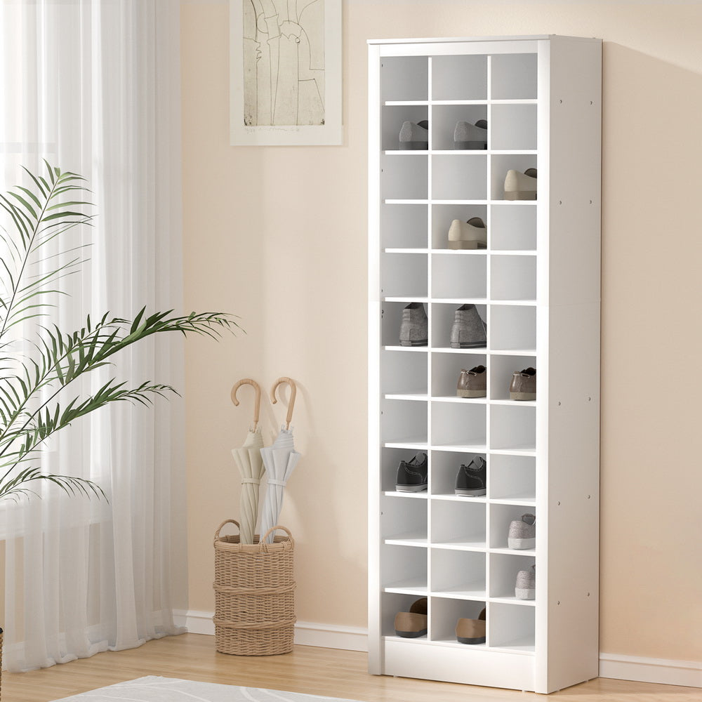 White open-slot shoe cabinet in hallway with peach walls, umbrella stand and plant beside