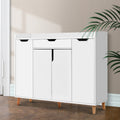 White shoe cabinet with top drawer three lower hinged doors and natural wood cone legs in hallway with herringbone floor