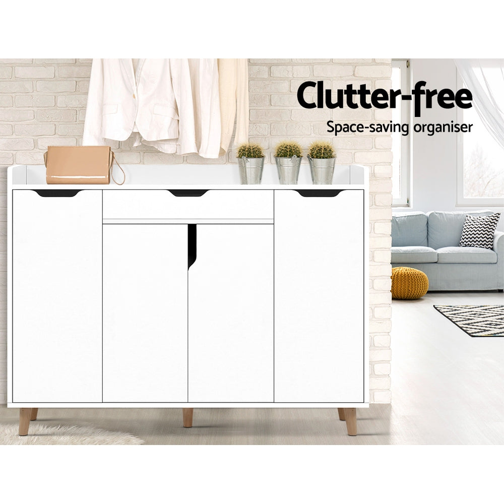White shoe cabinet all doors closed in living room lifestyle with exposed brick wall coats hanging on wall clutter-free text