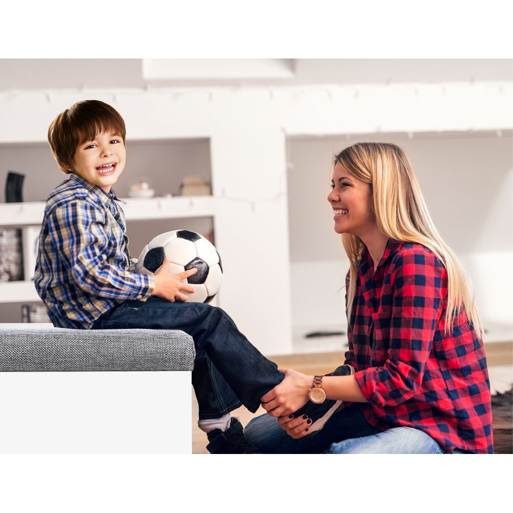 Child sitting on white storage bench grey cushion holding soccer ball with woman beside lifestyle seating in use shot