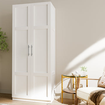 Tall white two-door storage cabinet with shaker panels and chrome handles in living room, glass side table and armchair