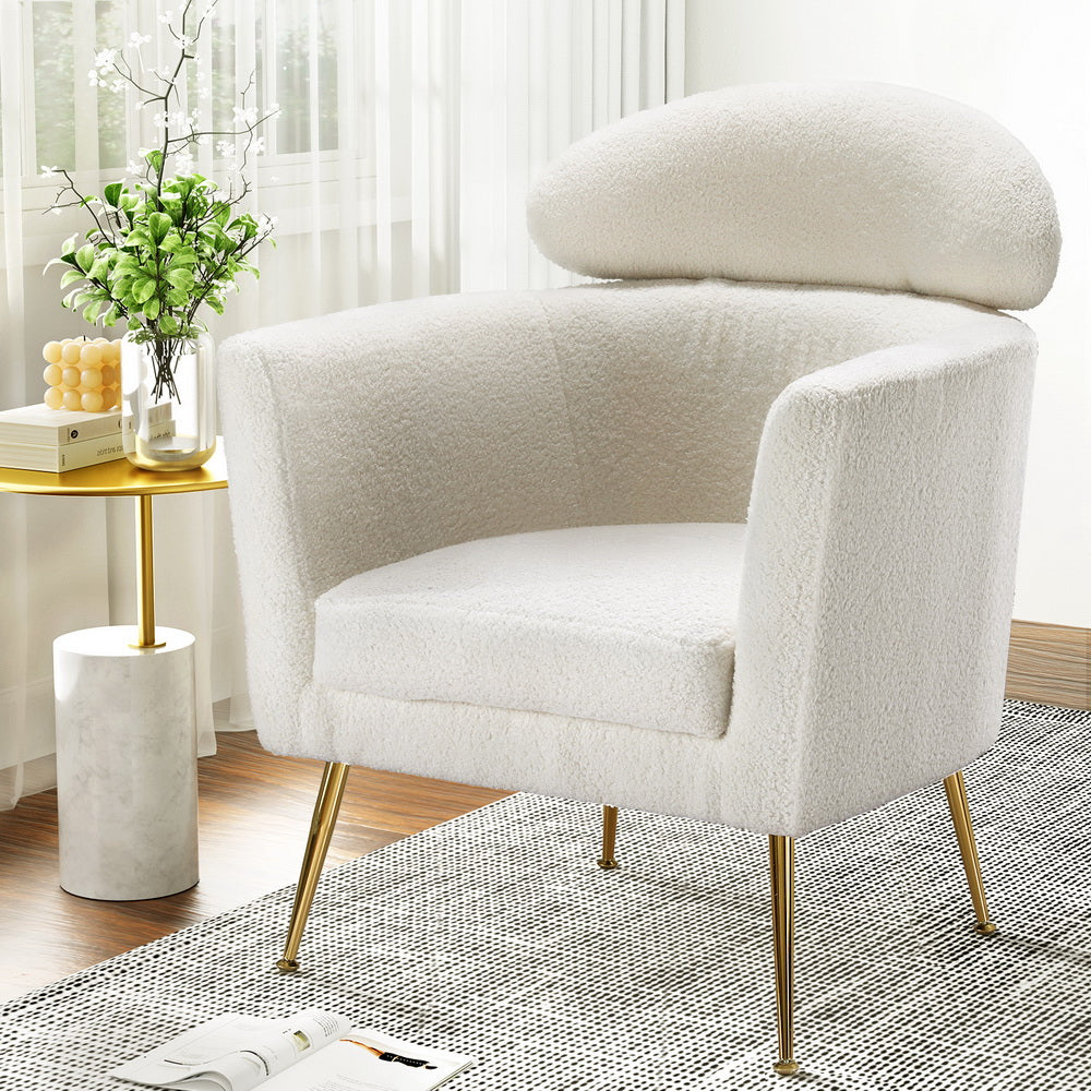 White teddy fabric barrel armchair with oval headrest pillow and gold metal legs, room with marble side table and flowers