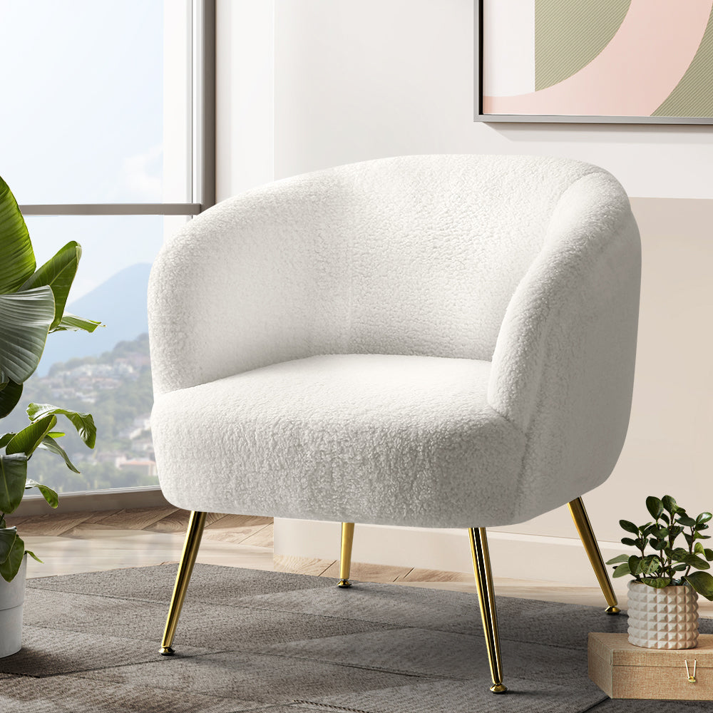 White teddy fabric barrel armchair with splayed gold metal legs in lifestyle room with large tropical plant and abstract art