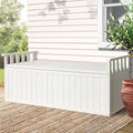 White timber outdoor storage bench on patio deck with woven rug, weatherboard wall and terracotta pot in background