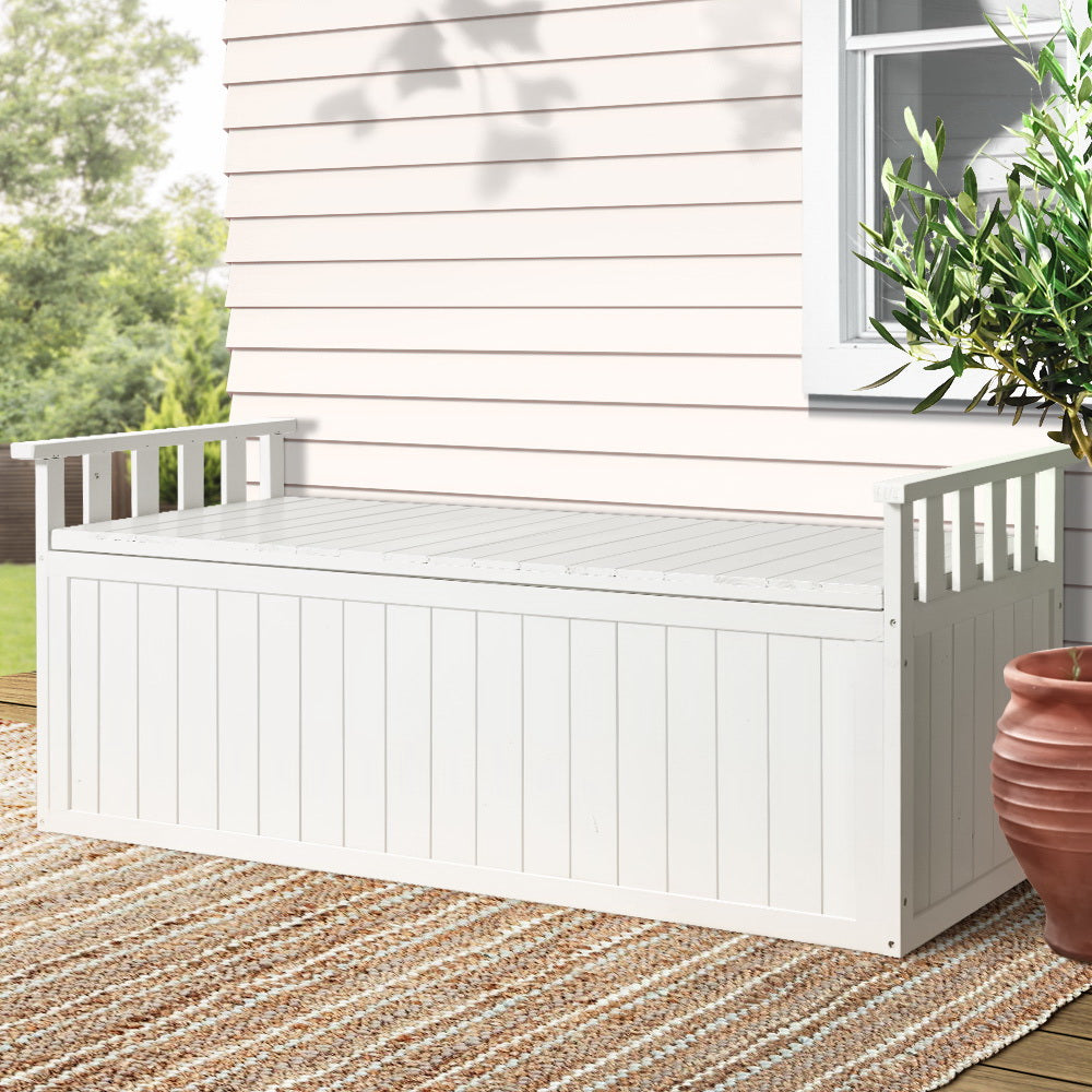 White timber outdoor storage bench on patio deck with woven rug, weatherboard wall and terracotta pot in background