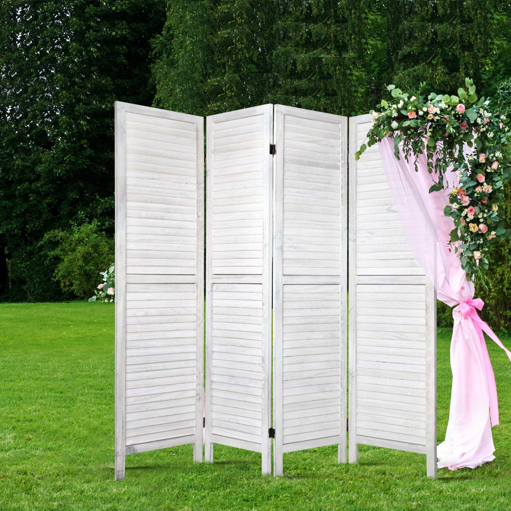 White-washed 4-panel louvered wood room divider outdoors in garden with green grass and pink floral arch drapery overhead