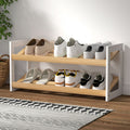 Two-tier shoe rack with white side panels and natural wood slatted shelves loaded with sneakers in room setting
