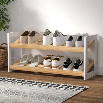 Two-tier shoe rack with white side panels and natural wood slatted shelves loaded with sneakers in room setting