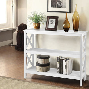 White console table with X-frame sides and two open shelves in room; styled with plant, photo frame, amber vases and books