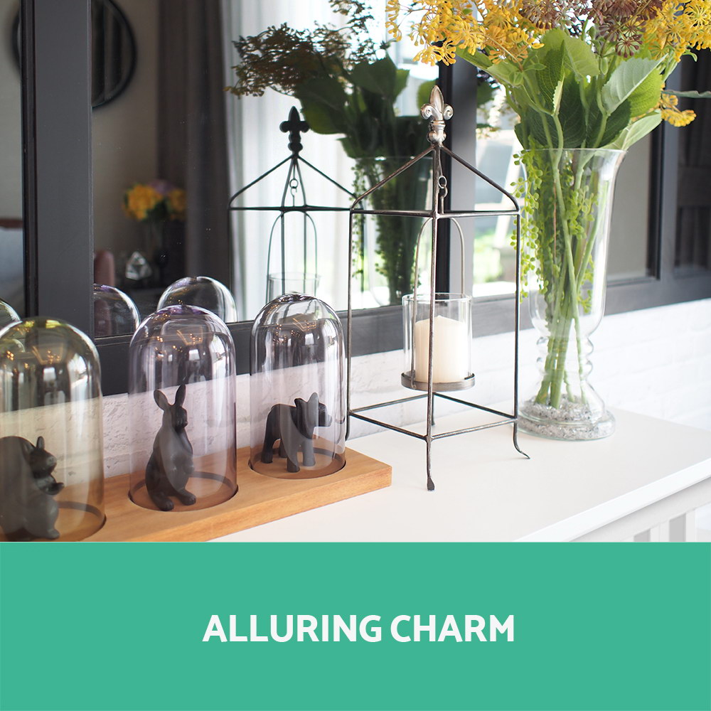 White console table top with glass cloches, animal figurines, cage lantern and flower vase; text "Alluring charm"